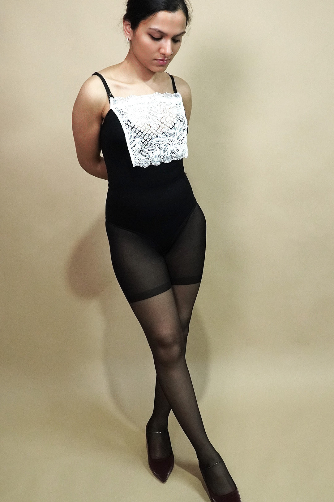 full length pose of woman wearing white lace camisole insert over black bodysuit on beige background, showing how mock lace panel adds neat coverage to deep neckline – muselot