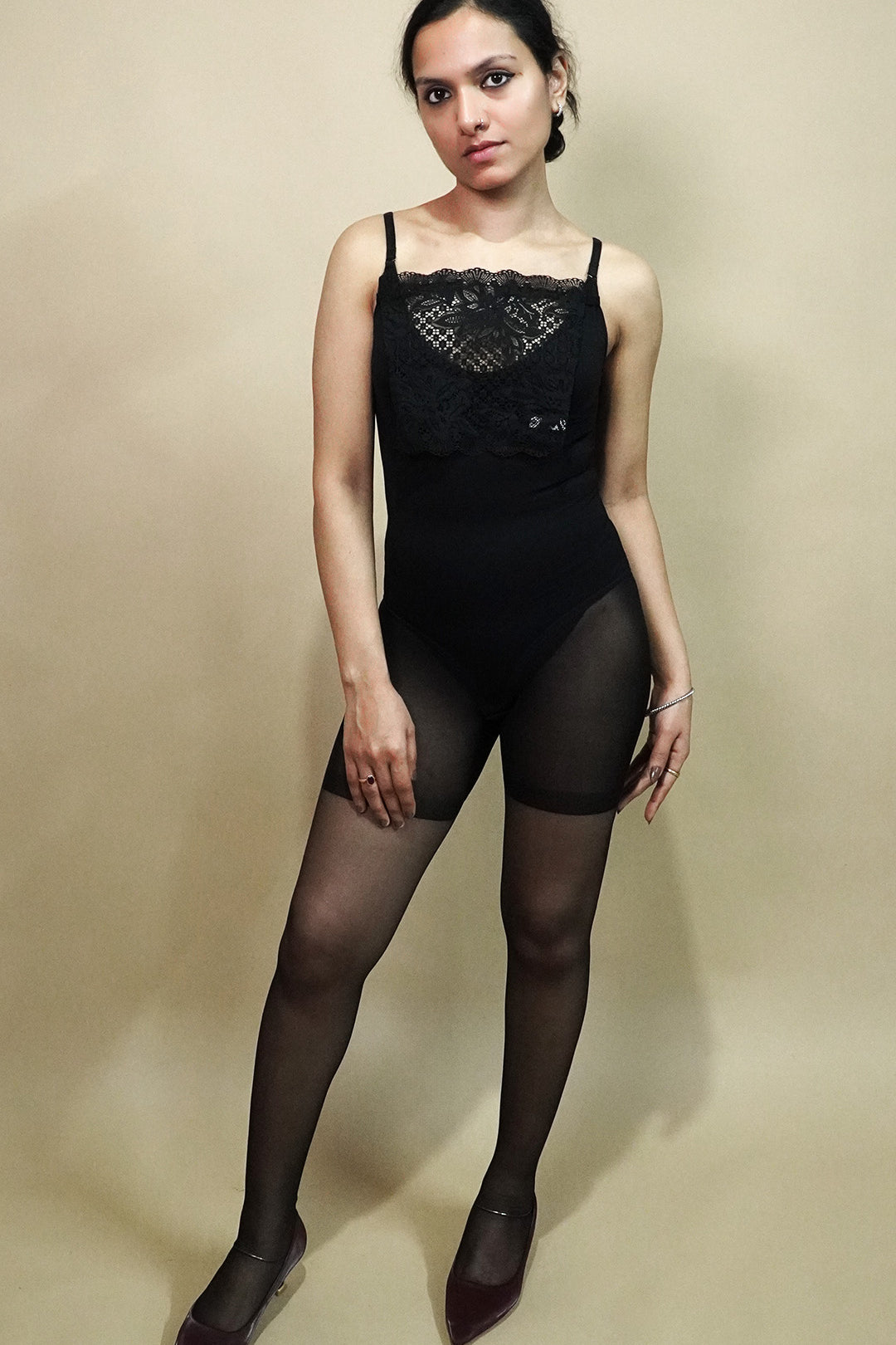 full body view of woman wearing black lace camisole insert over black outfit on beige background, showcasing elegant deep neckline styling with sheer floral lace mock camisole for layered look – muselot