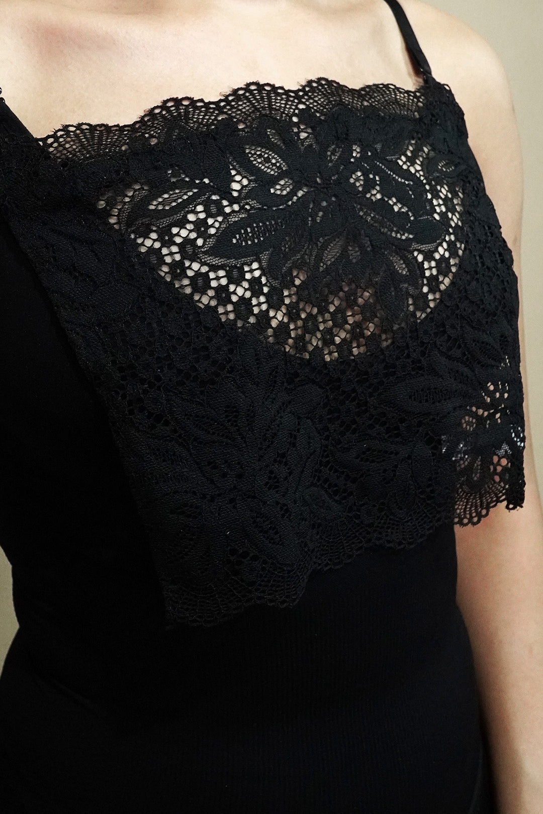 Side-angled close up of woman wearing black lace mock camisole over black top on beige background, showcasing wide lace panel that enhances neckline styling while keeping the look balanced – muselot