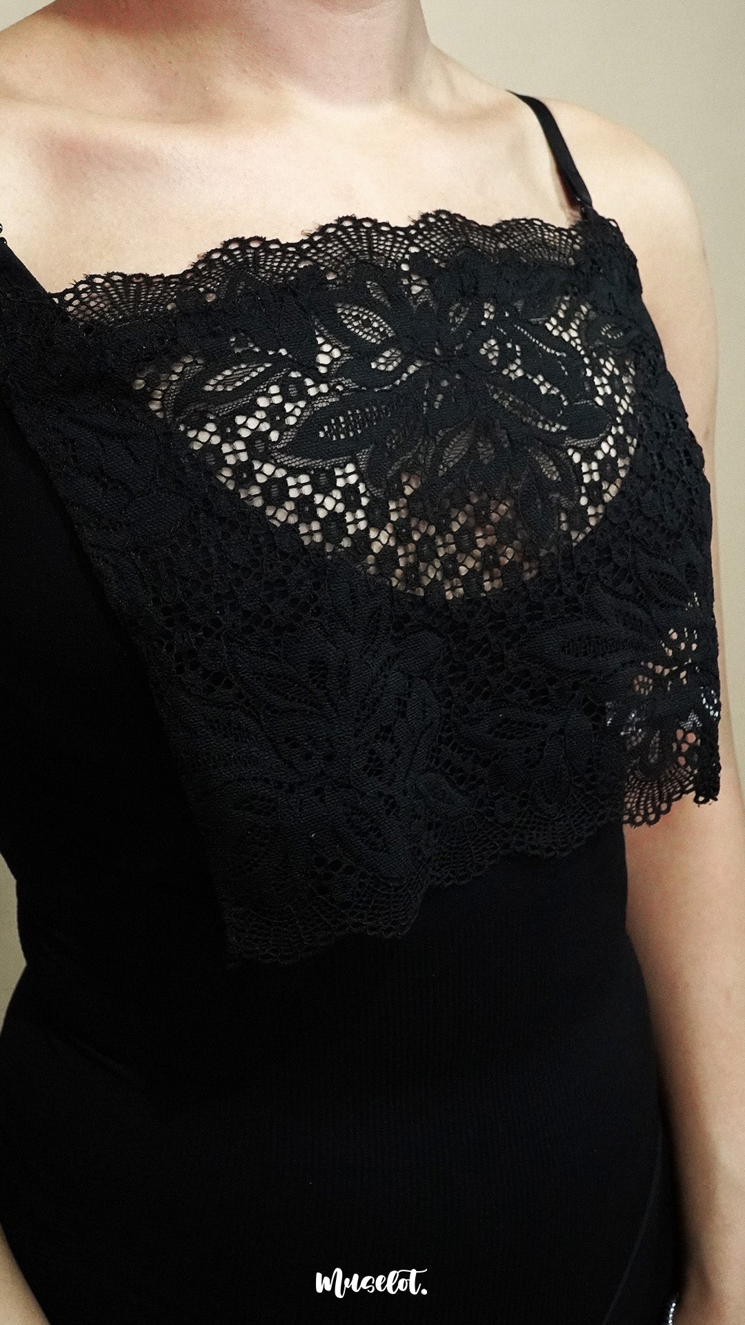 Side-angled close up of woman wearing black lace mock camisole over black top on beige background, showcasing wide lace panel that enhances neckline styling while keeping the look balanced – muselot