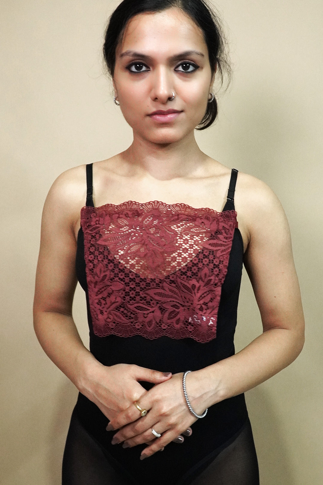 A front view of woman wearing burgundy lace camisole insert over black top on plain beige background, showcasing deep neck cover up and cleavage cover for low neckline dresses