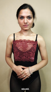 A front view of woman wearing burgundy lace camisole insert over black top on plain beige background, showcasing deep neck cover up and cleavage cover for low neckline dresses