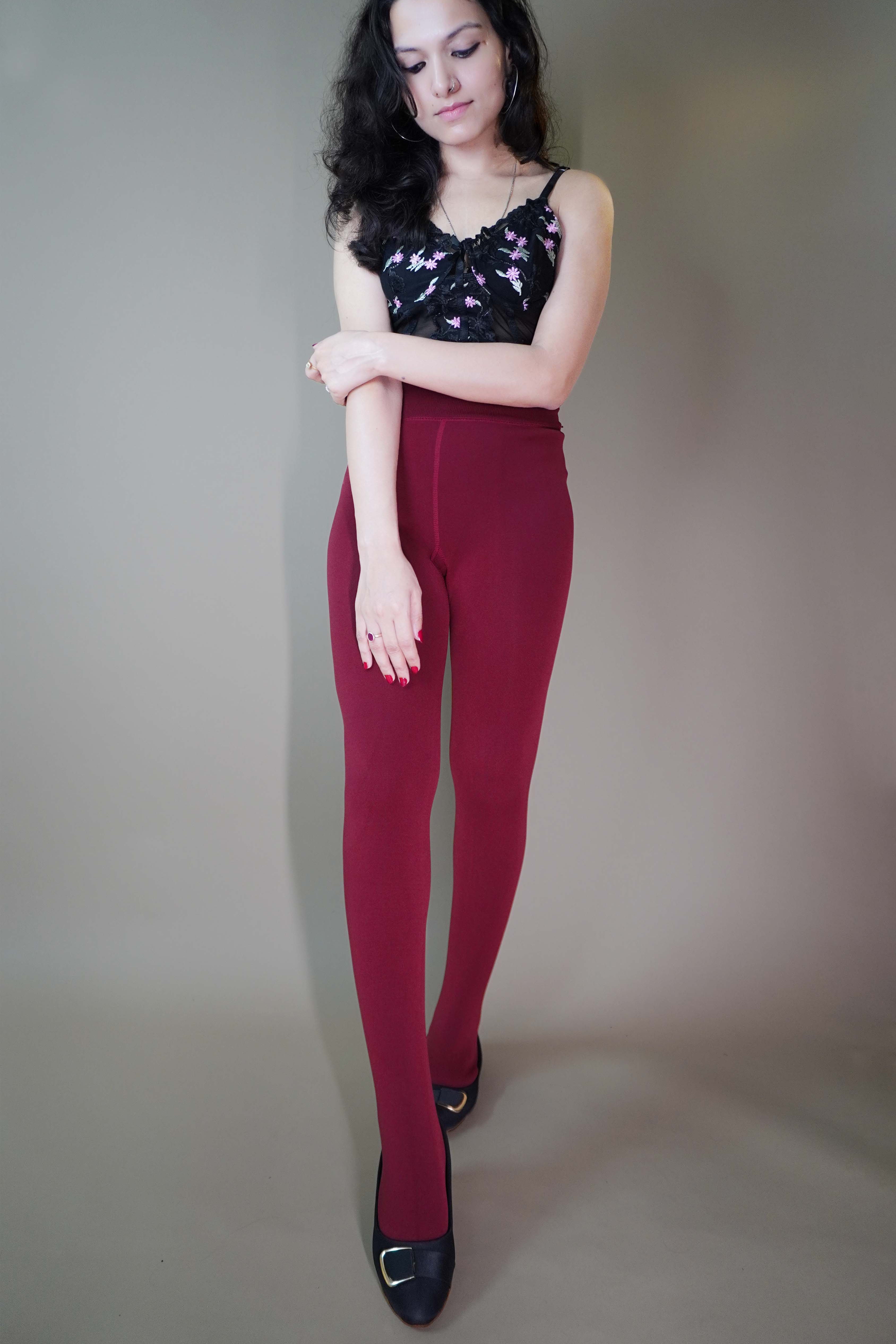 A model, wearing comfy warm berry maroon tights, is showcasing their soft, cozy fabric that provides a perfect balance of comfort and warmth. The rich berry maroon color highlights a stylish and practical design, ideal for layering or wearing solo. -Muselot