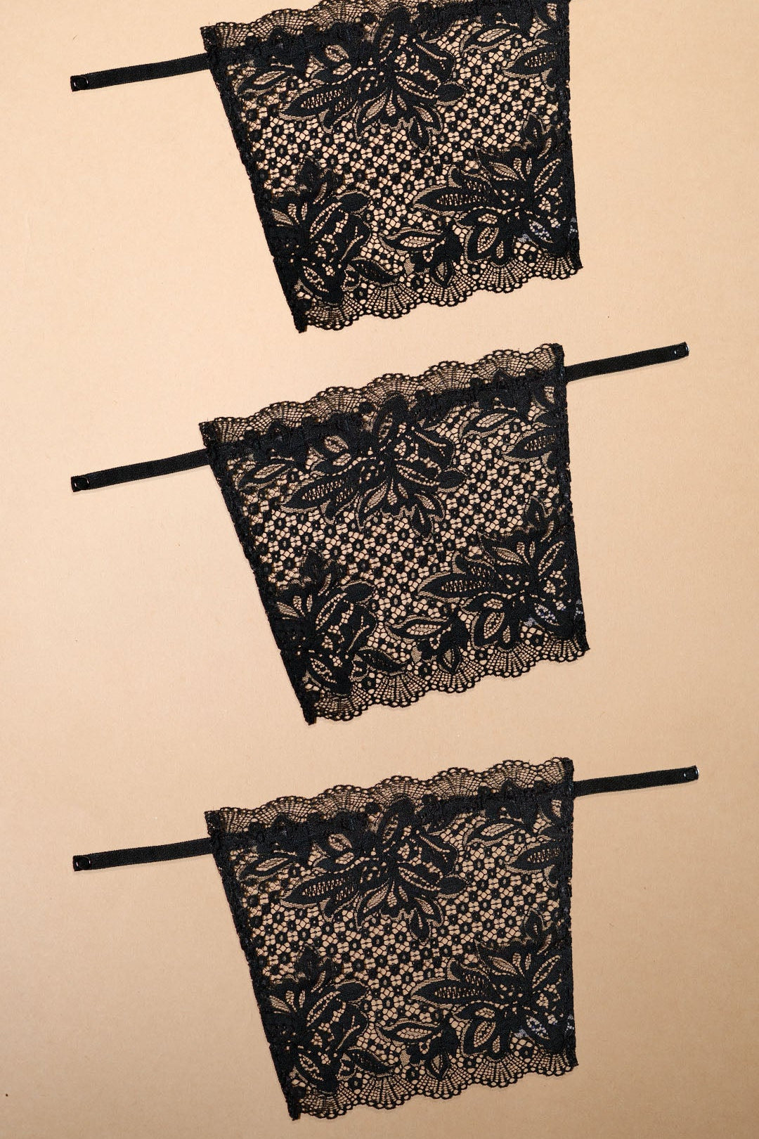 Three black lace clip-on neckline covers displayed on a beige background, featuring intricate floral lace patterns, adjustable straps and elegant scalloped edges. Designed for deep neck tops, dresses and blouses, these lightweight mock camisole inserts provide customizable neckline coverage while adding a sophisticated layered look with comfort and versatility – Muselot