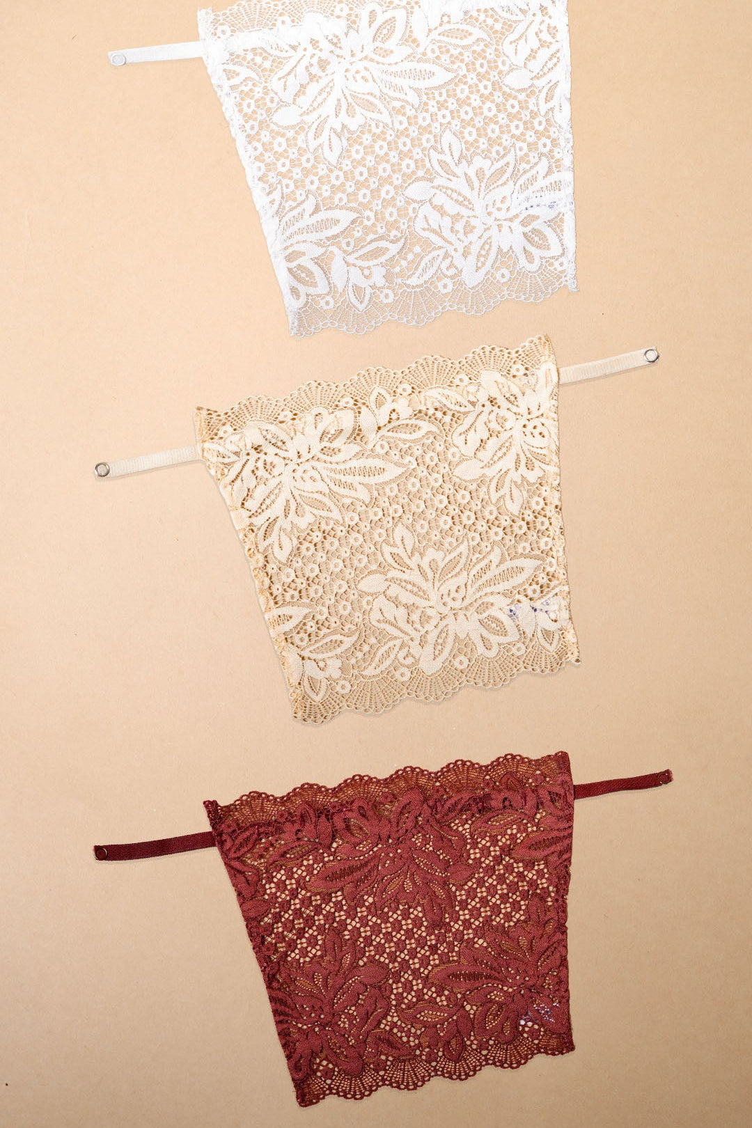 A pack of 3 deep neck cover-up displayed on a beige background, featuring white, beige and burgundy lace neckline inserts with premium floral lace detailing, adjustable straps and elegant modesty coverage for deep neck tops, blouses and dresses-Muselot