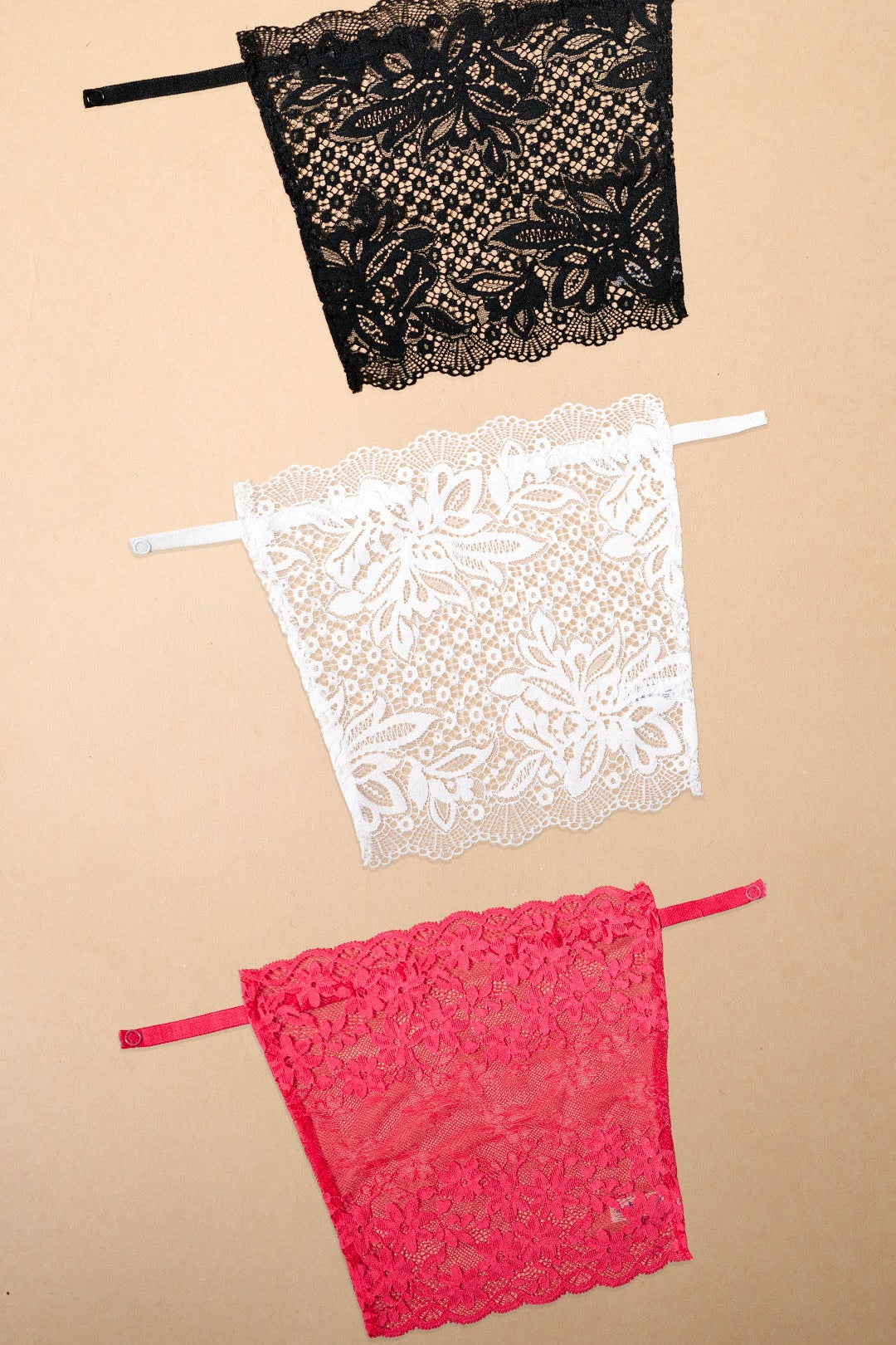Three lace neckline cover-ups in black, white and dark pink displayed on a beige background, showcasing vibrant colour choices, intricate floral lace patterns and elegant styling options for deep neck tops, dresses and blouses – Muselot