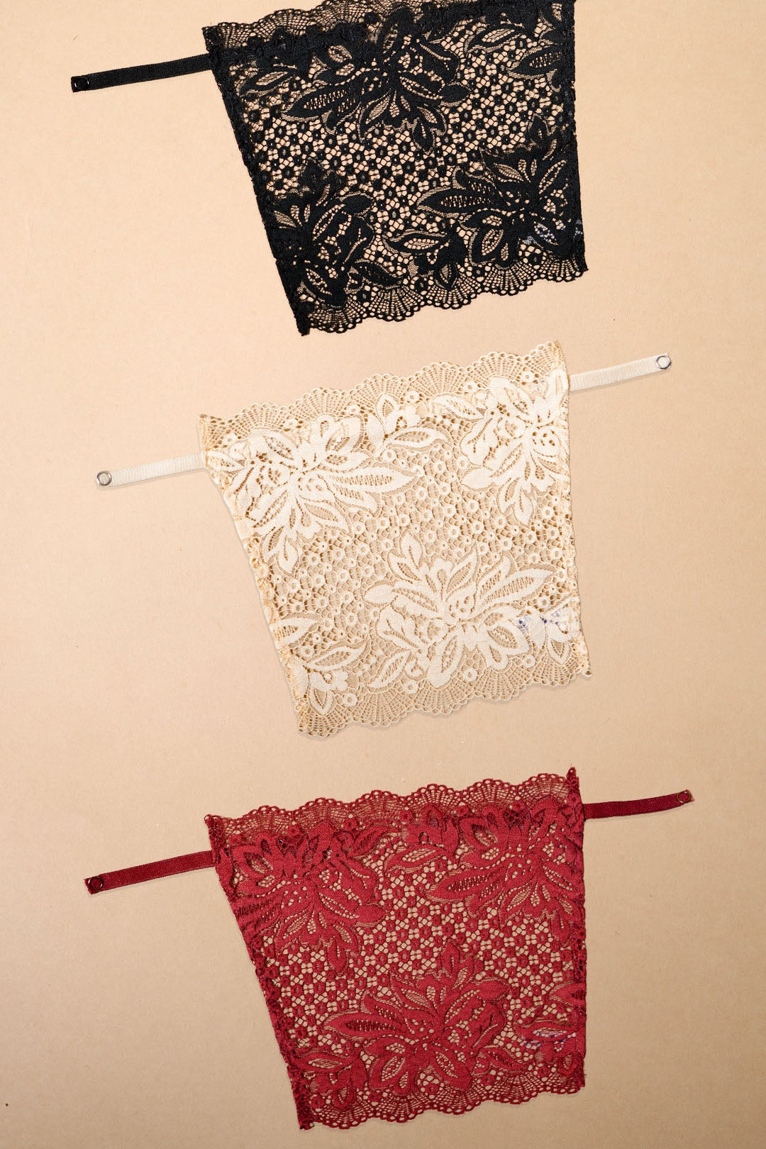 A pack of three clip-on neckline covers in black, beige and maroon is displayed on a beige background. Crafted from premium floral lace with adjustable straps and delicate scalloped edges, these deep neck cover-ups pair beautifully with dresses, tops, blouses and kurtis. The lightweight clip-on camisole inserts provide elegant neckline coverage, effortless layering and versatile styling, helping create a polished, confident look while enhancing the beauty of low-neck and deep-neck outfits – Muselot