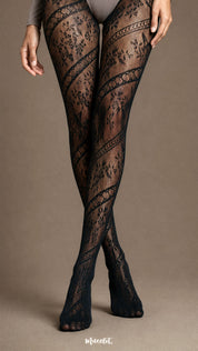 A product-focused view of crossed legs in black patterned stockings highlighting floral lace motifs, diagonal bands and sheer mesh texture - Muselot