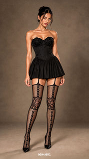 A woman wearing black fishnet garter stockings with a black corset mini dress and heels, showcasing the floral lace knee design, vertical heart motifs and elegant garter-style upper construction - Muselot