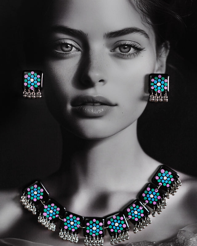 Model wearing handmade jewelry set with black hand-painted tiles featuring teal and purple motifs and silver ghungroo edging, styled to showcase the full necklace and earrings – Muselot.