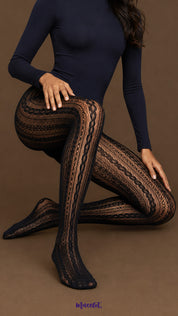 A model seated on the floor wearing black Heritage Braid designer lace stockings with elongated vertical motifs, intricate mesh work and full-leg coverage.