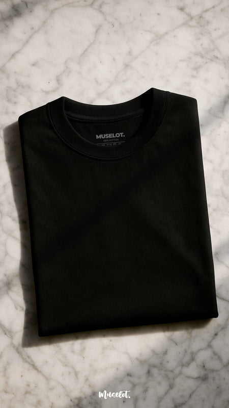 A unisex oversized black T-shirt is kept neatly folded on a sunlit marble surface, showcasing it's smooth texture and deep hue of the fabric, making it a bold yet minimal statement — Muselot.