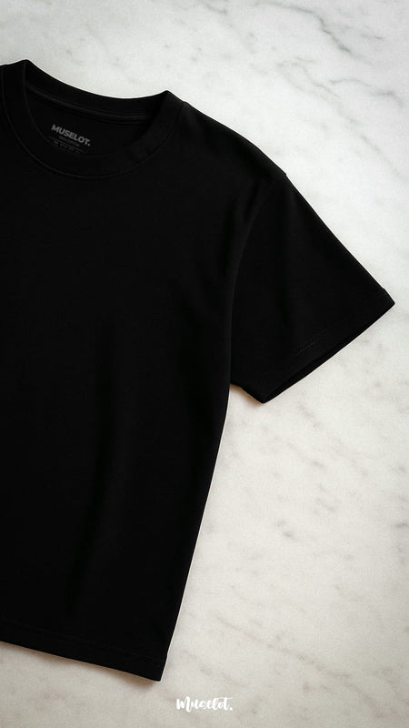 A half-flat lay shot of the unisex oversized black t-shirt placed on a sleek marble surface, showcasing its minimalist design and premium fabric—Muselot