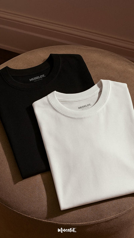 A flat lay shot of unisex oversized black and white t-shirt pair, kept neatly folded in a soft warm light highlighting the fabric’s texture and clean, minimalist design-Muselot