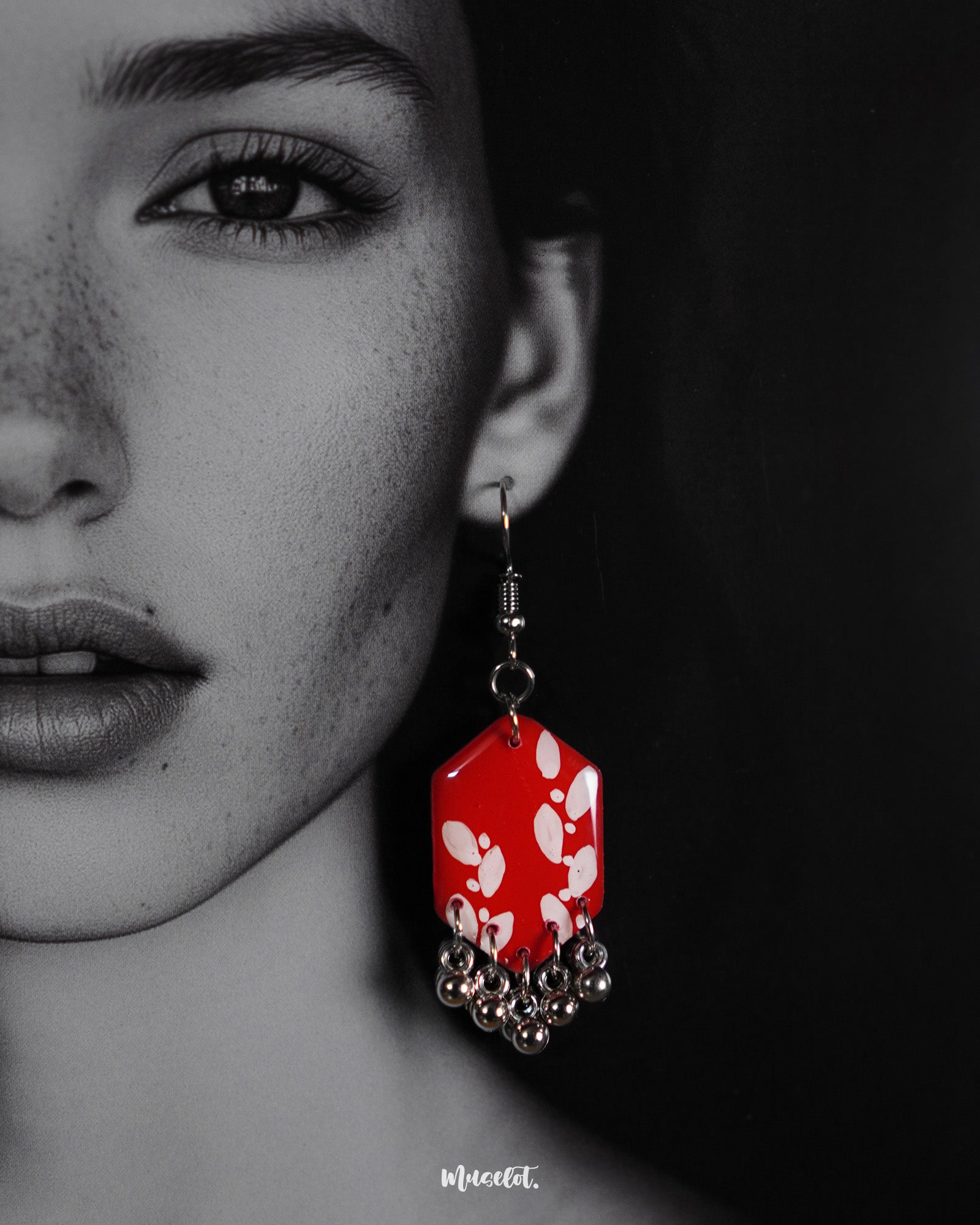 A close-up look at a model wearing the red hook earrings from Muselot — showcasing the vivid red enamel drops adorned with delicate metallic accents, highlighting the intricate craftsmanship and bold fusion of tradition with modern charm.
