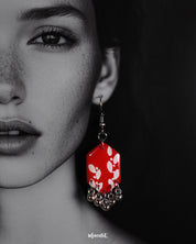 A close-up look at a model wearing the red hook earrings from Muselot — showcasing the vivid red enamel drops adorned with delicate metallic accents, highlighting the intricate craftsmanship and bold fusion of tradition with modern charm.