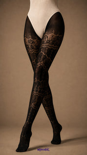 A focused view of crossed legs wearing full-length black lace stockings with intricate ornate motifs, semi-sheer sections and covered toes - Muselot