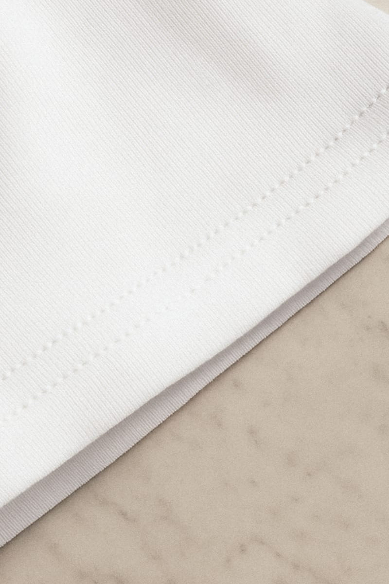 Close-up shot of an unisex oversized white t-shirt, showcasing the intricate fabric stitching,  and highlighting its premium texture and rich craftsmanship— Muselot.